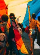 Groupe de personnes en manifestation sous un drapeau arc en ciel // Source : Mercedes Mehling / Unsplash
