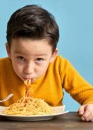 Un enfant en pull jaune en train de manger un plat de pâtes au ketchup // Source : pinstock de Getty Images Signature